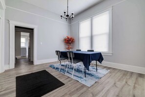 Een eetgedeelte met een tafel gedekt voor vier personen, een kroonluchter en een groot raam met zonwering.