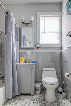 A bathroom with a toilet, sink, shower curtain, and a window.