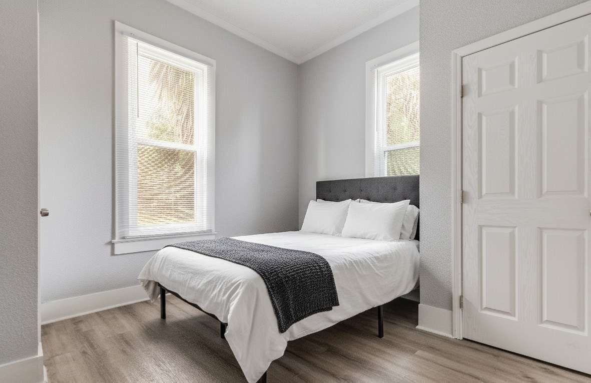 Un dormitorio con una cama, dos ventanas y una puerta.