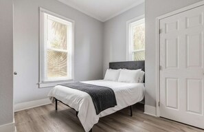 Een slaapkamer met een bed, twee ramen en een deur.