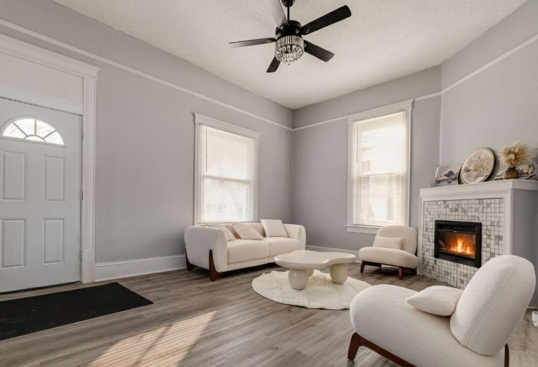 A living room with a fireplace, a ceiling fan, and a large window.