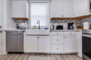 Une cuisine moderne avec des meubles blancs, un lave-vaisselle, un évier avec un robinet, une machine à café et un grille-pain.