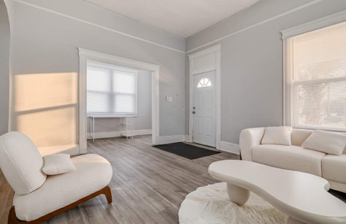 Een ruime woonkamer met een groot raam, een witte bank, een fauteuil en een salontafel.