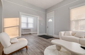 A spacious living room with a large window, a white sofa, a chair, and a coffee table.