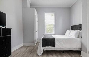 A bedroom with a bed, a television, a wardrobe, and a window with blinds.