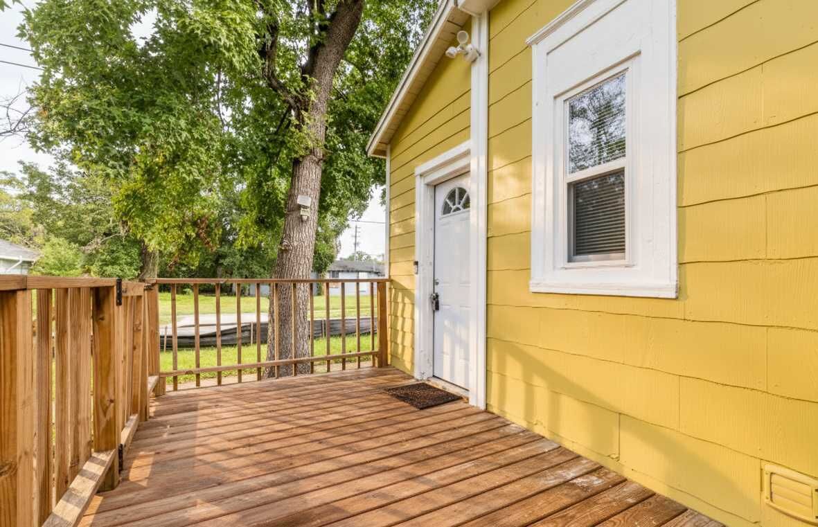 Una casa amarilla con una terraza de madera, una puerta blanca y una ventana.