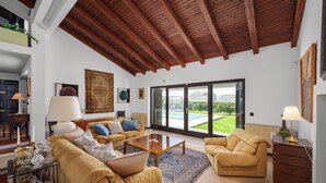 A spacious living room with a high ceiling, a large window offering a view of a green landscape, and a cozy seating area with a coffee table.