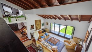 A spacious living area with a high ceiling, a sofa set, a coffee table, and a view of the outdoors through large windows.
