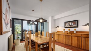 A dining area with a wooden table, chairs, pendant lights, a radiator, and a large window.
