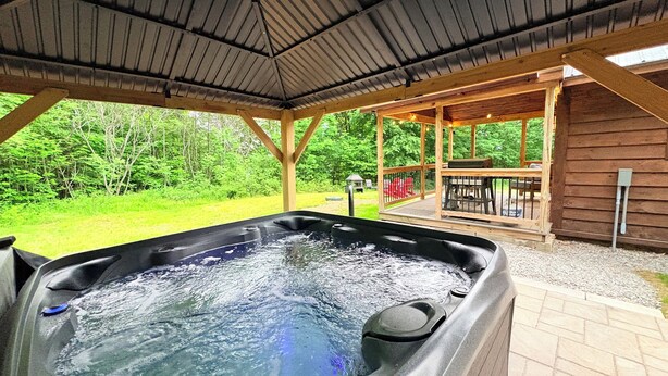Un jacuzzi con cubierta de madera y zona techada, rodeado de follaje.