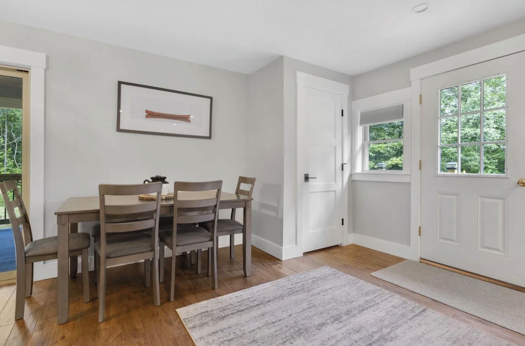 A dining area with a table and chairs, a framed picture on the wall, and a door leading outside.