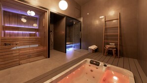 Un espace spa moderne doté d’un grand jacuzzi, d’un sauna en bois et d’un hammam à parois de verre.