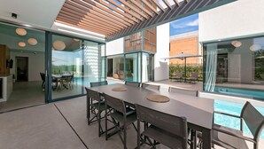 Un espace de restauration extérieur moderne, doté d’une piscine, de murs en verre et d’une structure de plafond en bois.