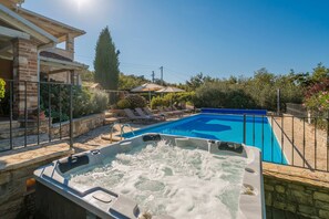 A swimming pool with a hot tub in the foreground, surrounded by lounge chairs and a stone wall. - Villa Salvea (100391-K1) - Montizana (Montizana)