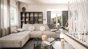 A modern living room with a sectional sofa, a glass coffee table, and a bookshelf.