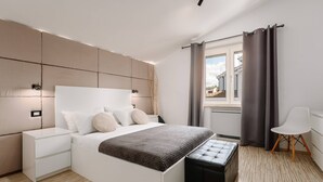 A modern bedroom with a large bed, bedside tables, a bench, and a view of the outside through a window.