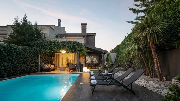 A swimming pool with lounge chairs, a patio area, and a building with a covered seating area.