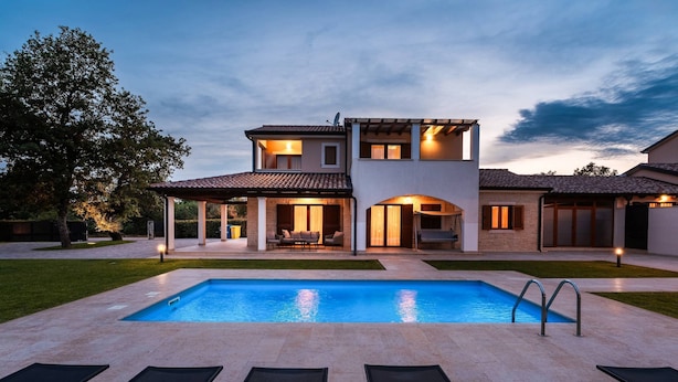 A modern two-story house with a swimming pool, outdoor seating, and a well-maintained lawn.