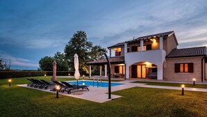 A modern house with a swimming pool, lounge chairs, and a covered patio area.