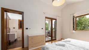A bedroom with a bed, a dresser, a bathroom with a sink, and a sliding glass door to a balcony.