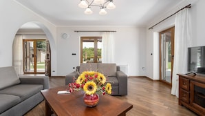 A modern living room with a sofa, a wooden coffee table with a vase of flowers, and a television on a wooden cabinet.