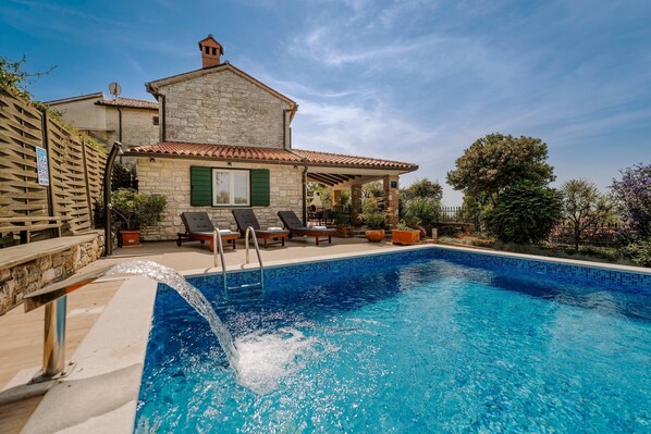 Une maison en pierre avec une piscine, un espace salon extérieur et une pergola.
