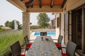 An outdoor patio with a table set for two, overlooking a swimming pool and a stone wall.