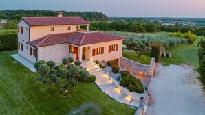 Une maison à deux étages, avec un toit recouvert de tuiles rouges, entourée d’une pelouse et d’un jardin bien entretenus.