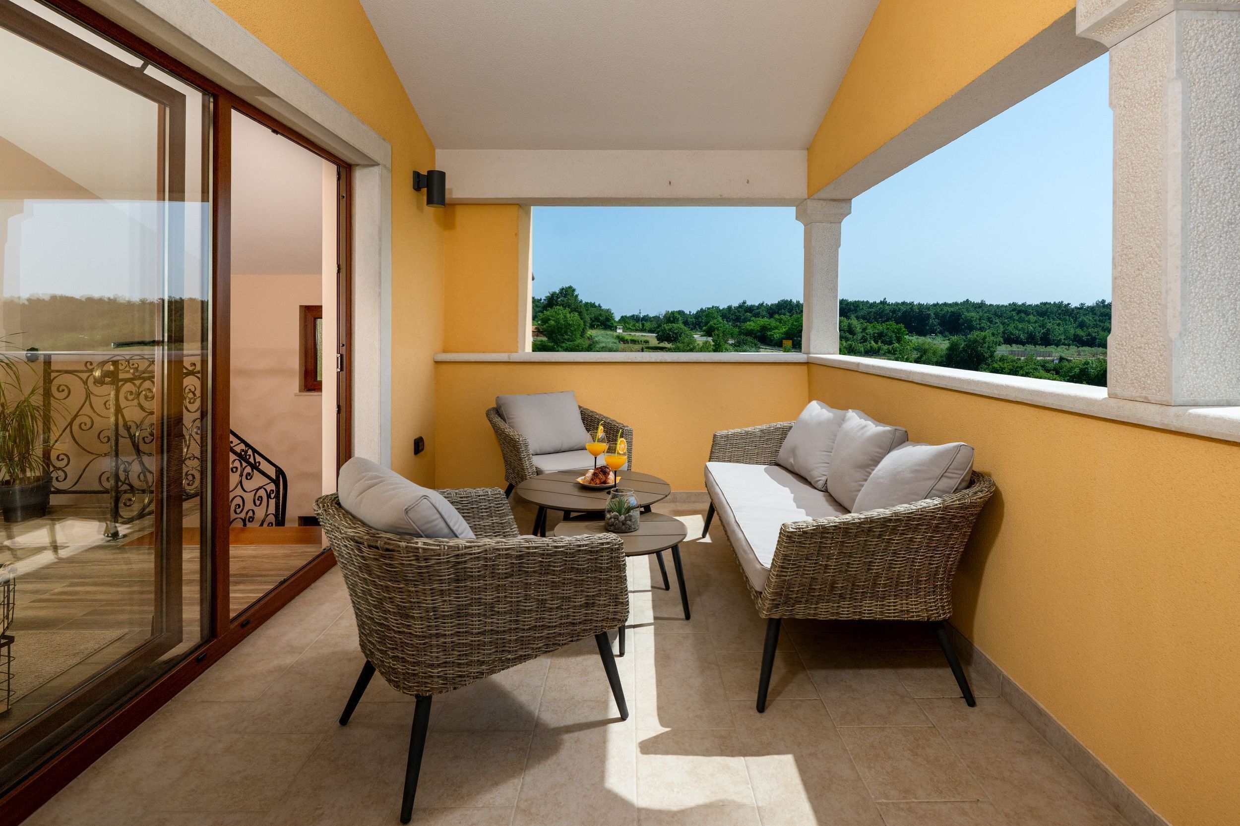 A balcony with wicker furniture, a glass door, and a view of greenery.