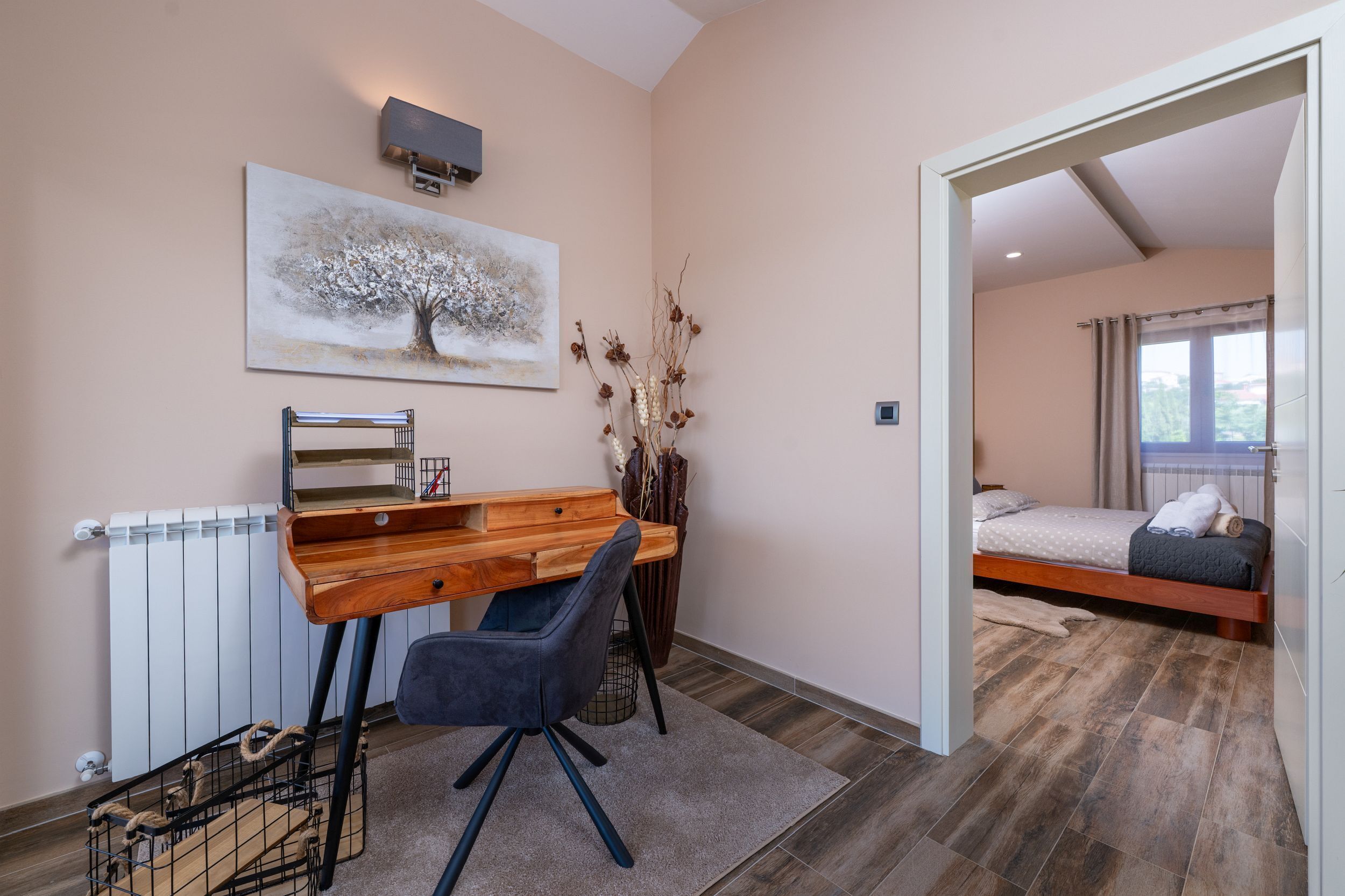 Une chambre à coucher avec un lit en bois, un bureau avec une chaise, un radiateur et un tableau représentant un arbre.