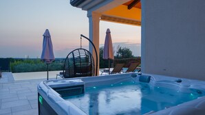 Un bain à remous avec vue sur le coucher de soleil, deux chaises longues et deux parasols.