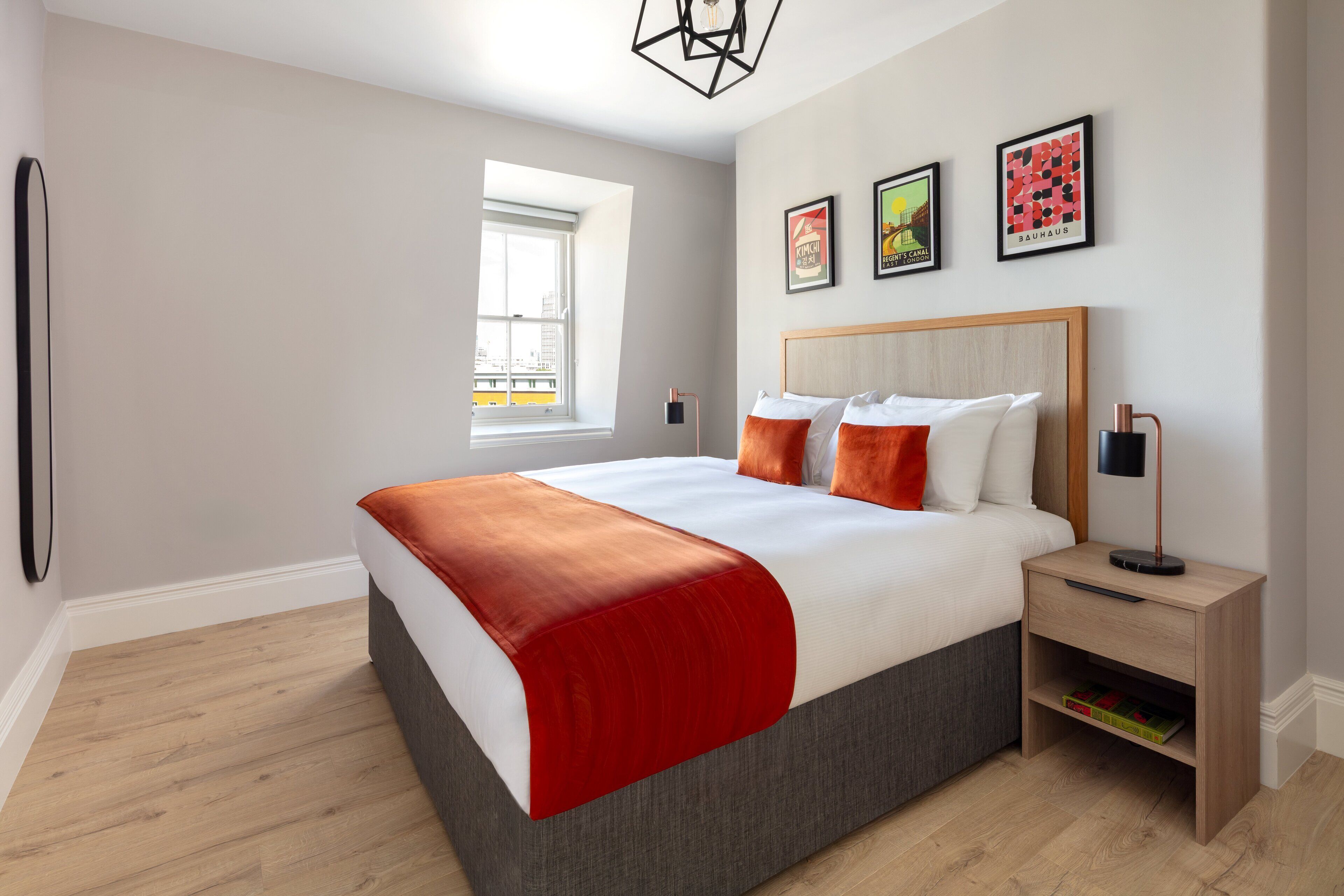 A modern bedroom with a large bed, a nightstand, a window, and three framed pictures on the wall.