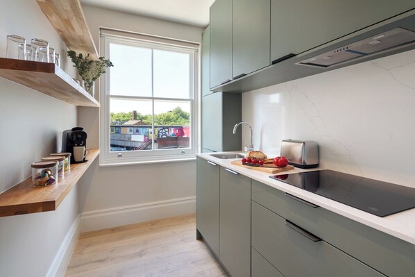 A modern kitchen with a built-in stove, a window, and wooden shelves.