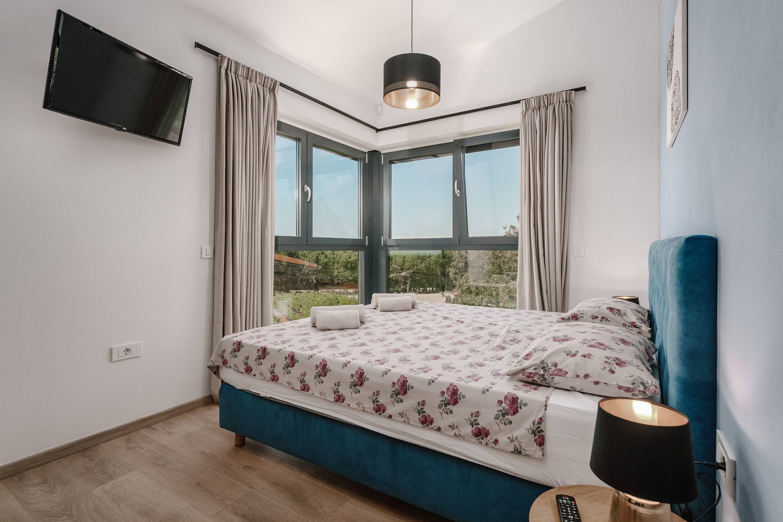 Un dormitorio con cama, televisor montado en la pared y ventana con cortinas.
