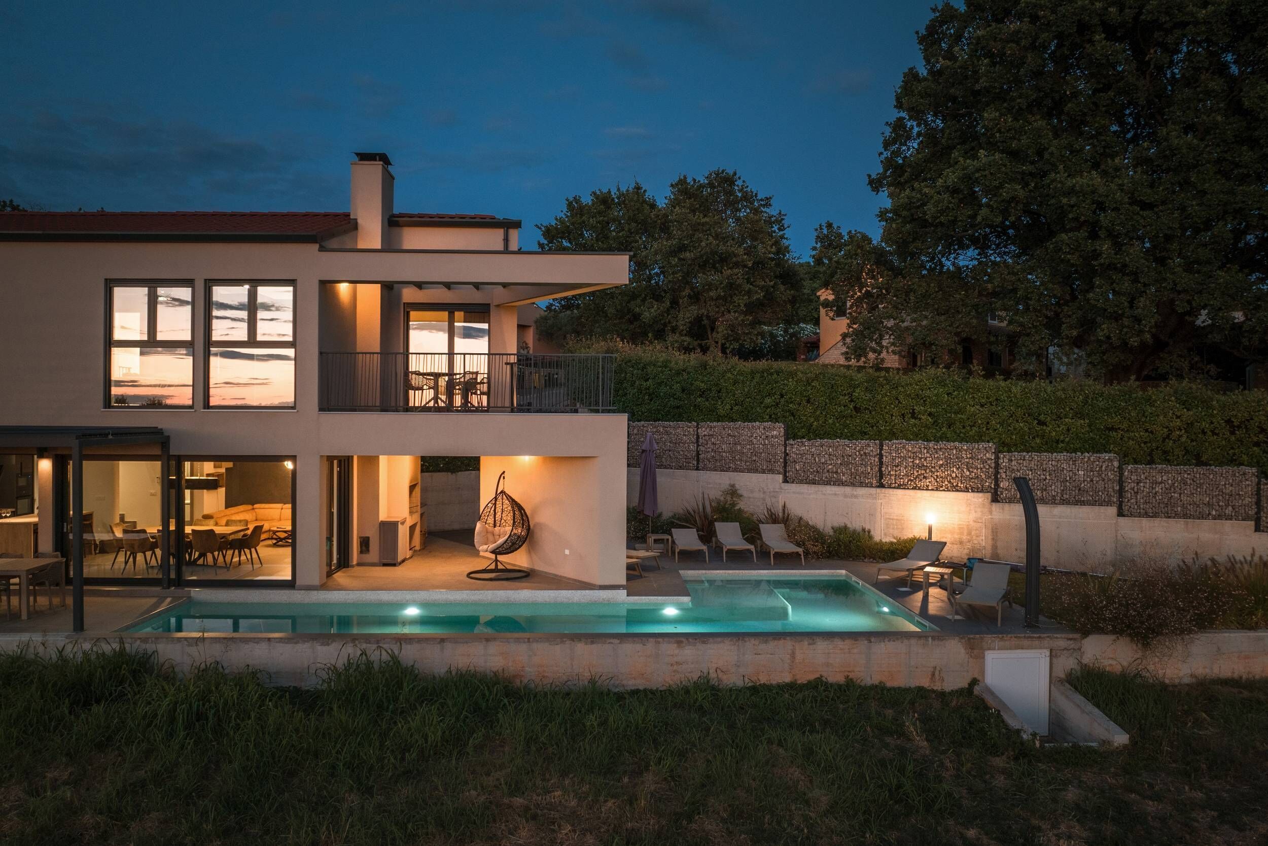 Ein modernes, zweistöckiges Haus mit Swimmingpool, Sitzgelegenheit im Freien und einem gepflegten Garten.