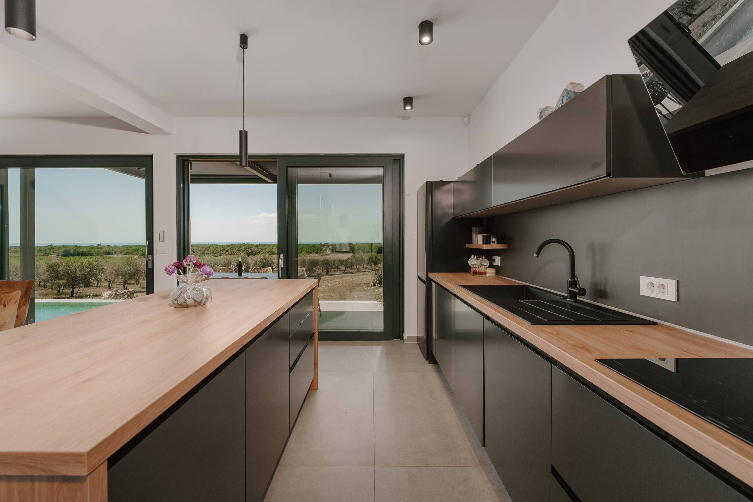 Una cocina moderna con encimera de madera, armarios negros y vistas al campo.