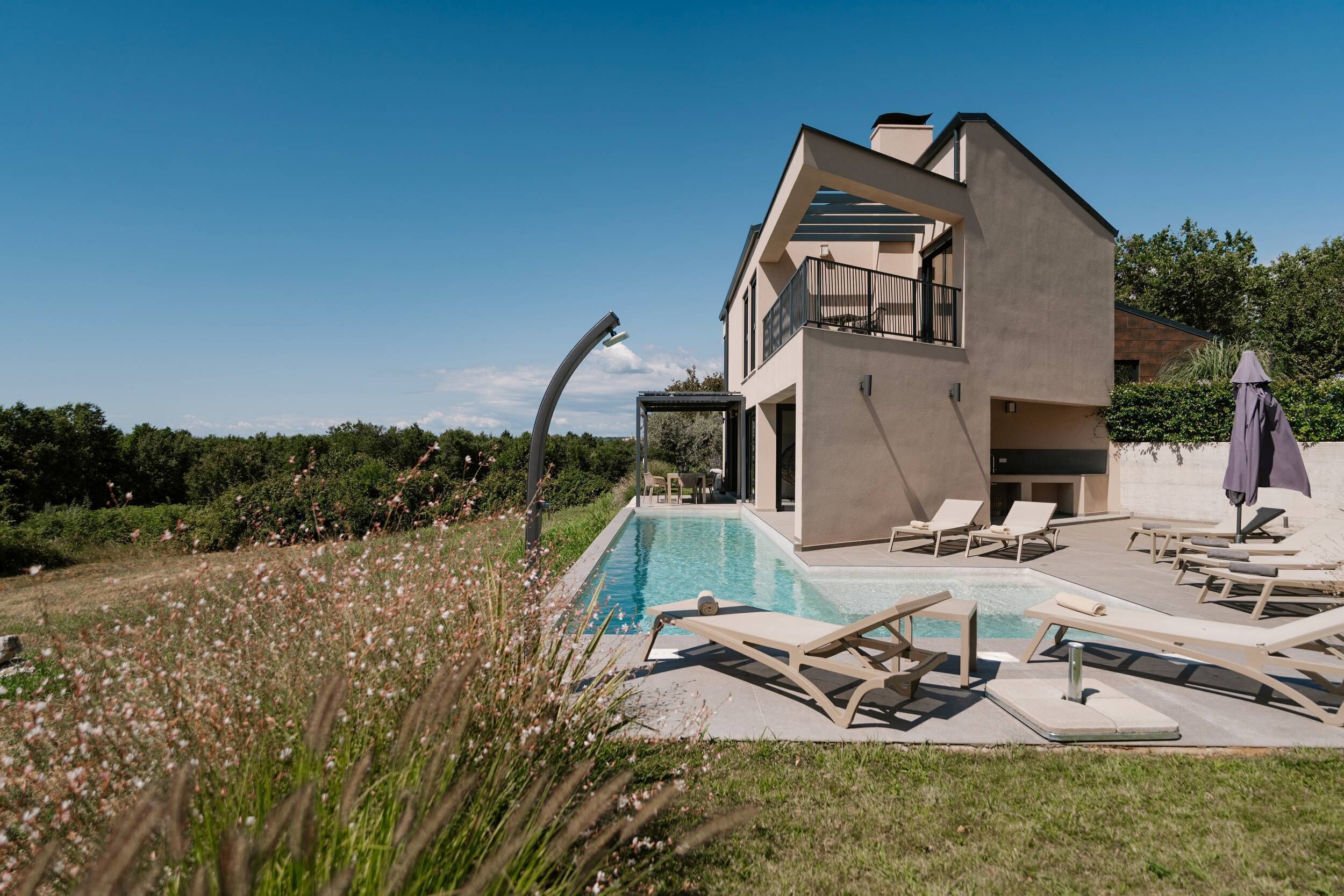 Une maison moderne à deux étages dotée d’une piscine, d’un espace salon extérieur et d’un jardin.