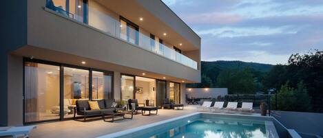 Una casa moderna de dos pisos con piscina, mobiliario exterior y vistas del paisaje circundante.