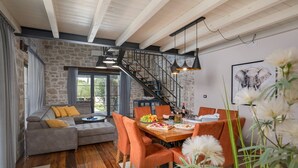 A modern living room with a stone wall, a wooden staircase, a dining area with orange chairs, and a large window.