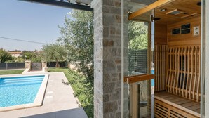 A stone exterior wall, a glass door leading to a sauna, and a swimming pool.
