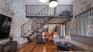 A spacious living area with a wooden floor, a large gray sofa, a coffee table, and a staircase leading to an upper level.