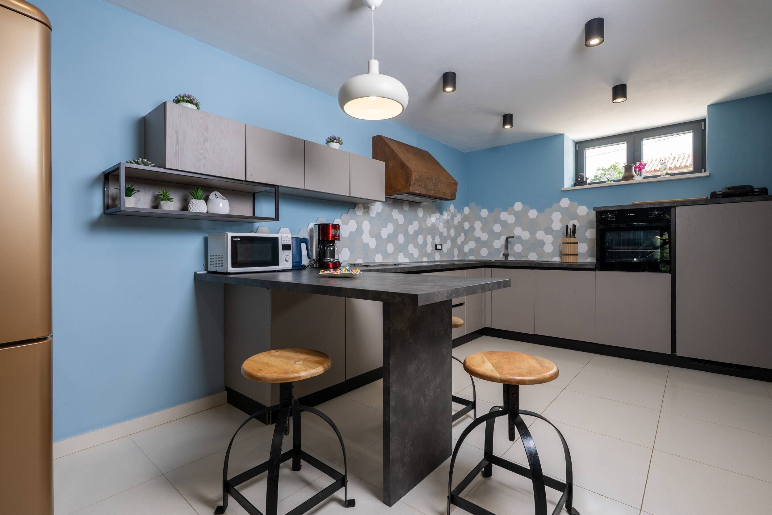 A modern kitchen with a central island, bar stools, a microwave, and a coffee maker.