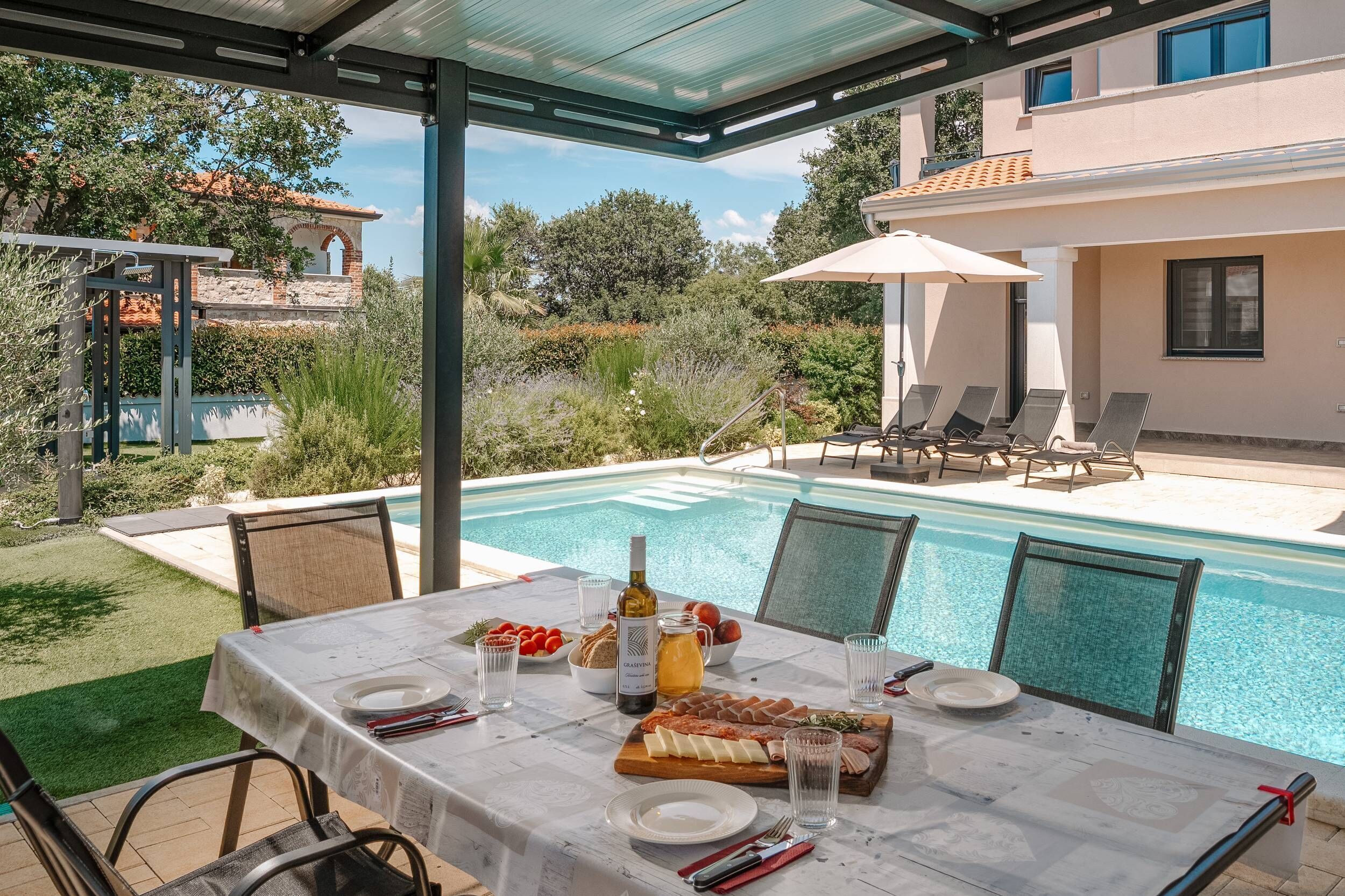 Un espace repas aménagé au bord de la piscine, avec une table dressée pour quatre personnes, entourée de chaises, d’une piscine et d’un patio couvert.