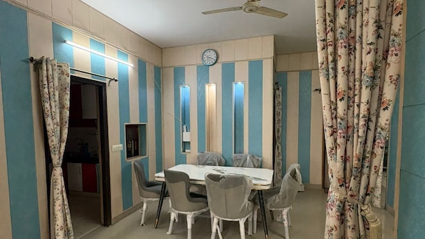 A dining area with a table and chairs, a ceiling fan, and striped walls. - Awaraj Home Stay (Agra)