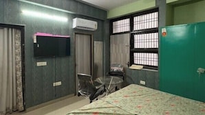 A room with a bed, a TV, a ceiling fan, a window with bars, and a green wardrobe. - Awaraj Home Stay (Agra)