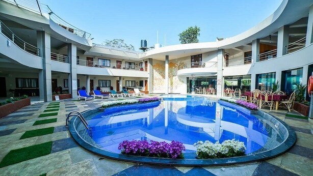 A modern hotel with a central swimming pool surrounded by lounge chairs and flower beds. - Ocean White Sands Resort & Spa (Varca)