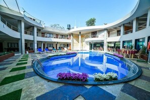 Un hôtel moderne doté d’une piscine centrale, entourée de chaises longues et de parterres de fleurs.