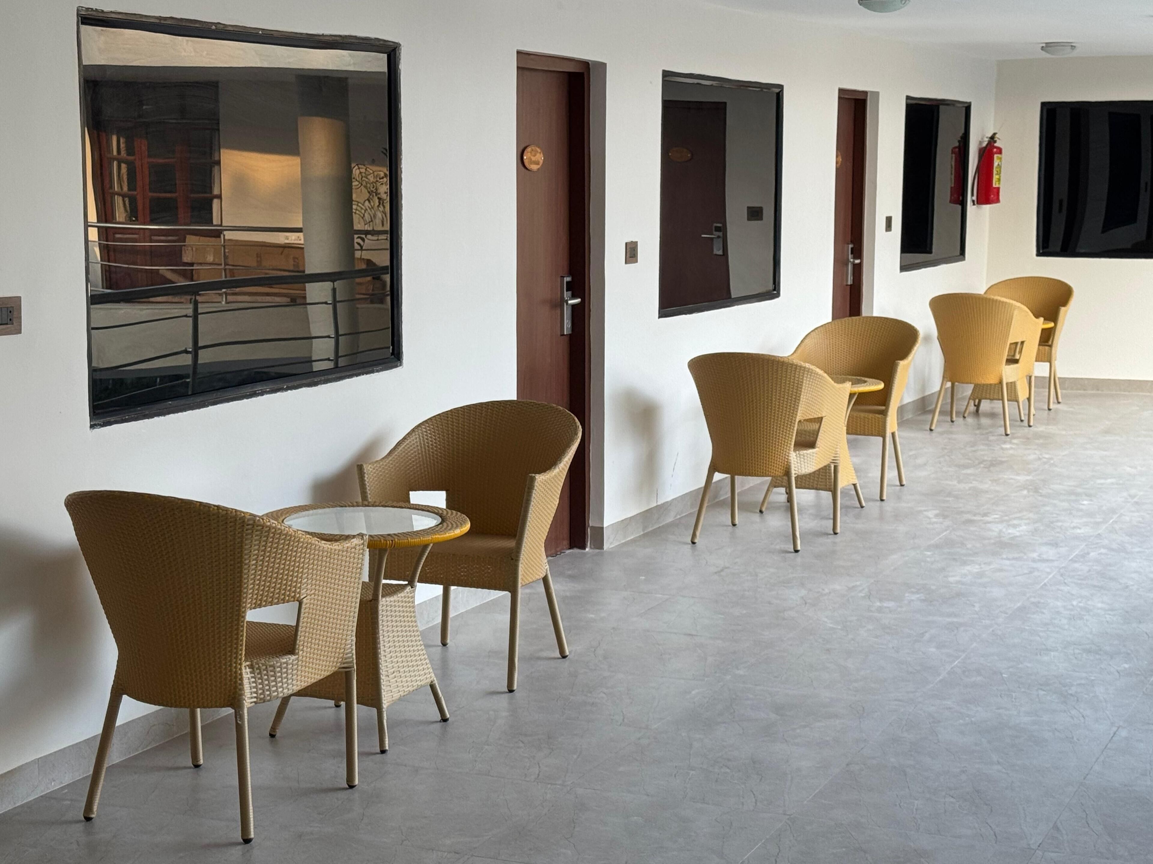 A corridor with wicker chairs and a small round table, doors, and a fire extinguisher on the wall.