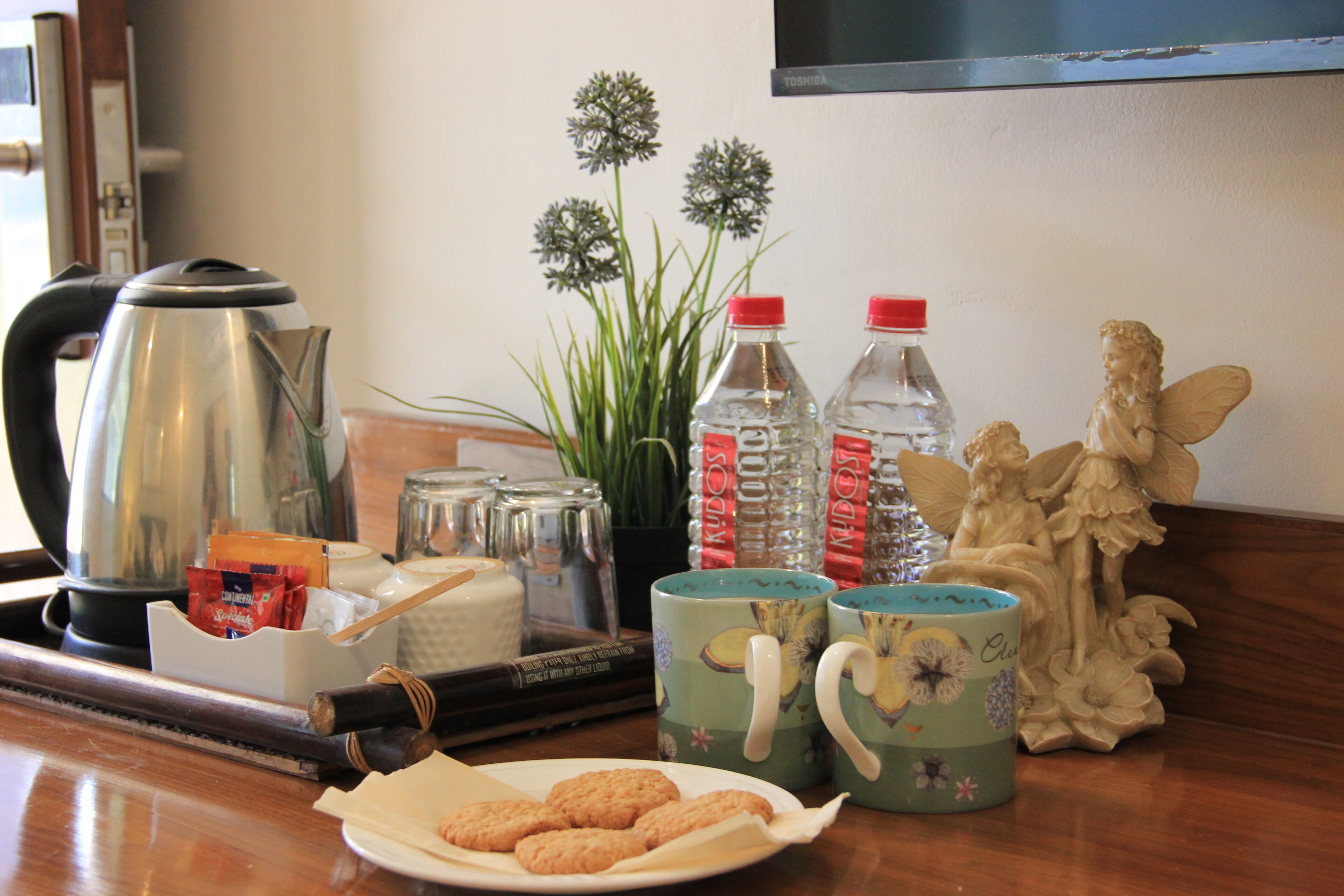 Una mesa con un plato de galletas, dos tazas, una tetera, una botella de agua y una estatua decorativa de un ángel.