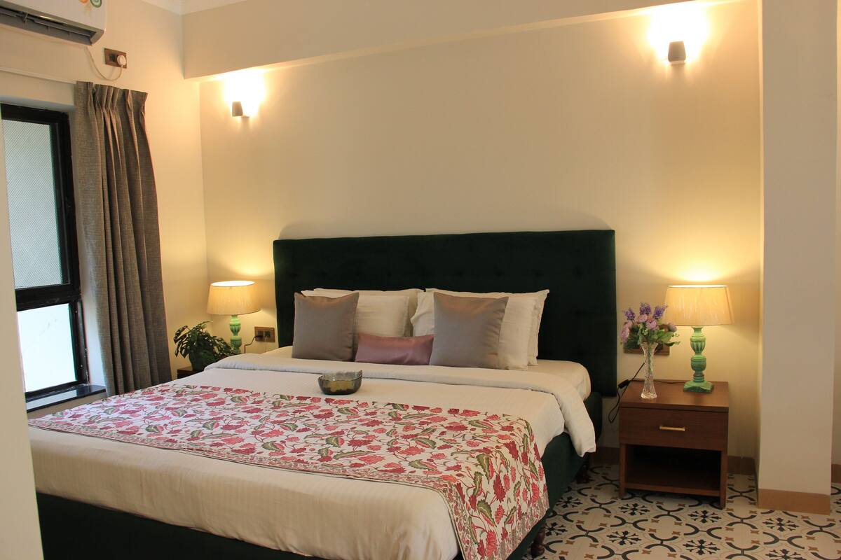 A neatly made bed with a floral bedspread, a green headboard, and two bedside lamps.